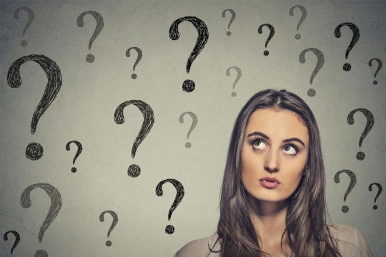 Ritratto che pensa a una giovane donna d'affari che guarda molti punti interrogativi isolati su sfondo grigio a parete