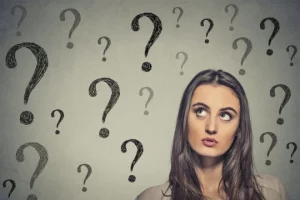 Portrait thinking young business woman looking up at many question marks isolated on gray wall background
